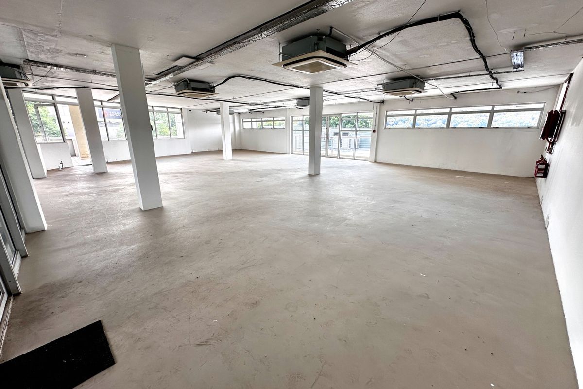 Spacious open-plan office area featuring exposed ceilings, cassette air conditioning, structural columns, and large windows providing ample natural light.