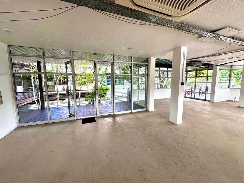 An open-plan office space featuring large aluminum-framed glass doors leading to an outdoor deck, exposed ceiling infrastructure, and a neutral, vacant layout.