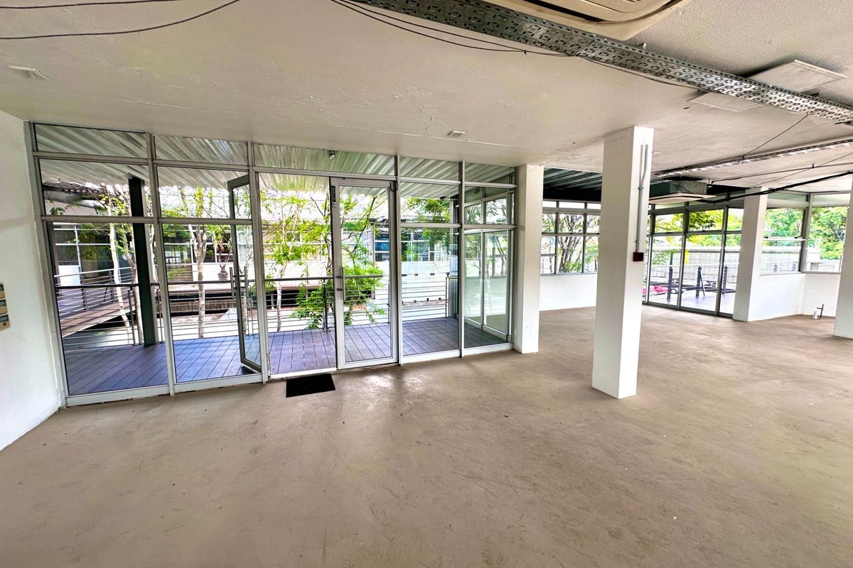 An open-plan office space featuring large aluminum-framed glass doors leading to an outdoor deck, exposed ceiling infrastructure, and a neutral, vacant layout.