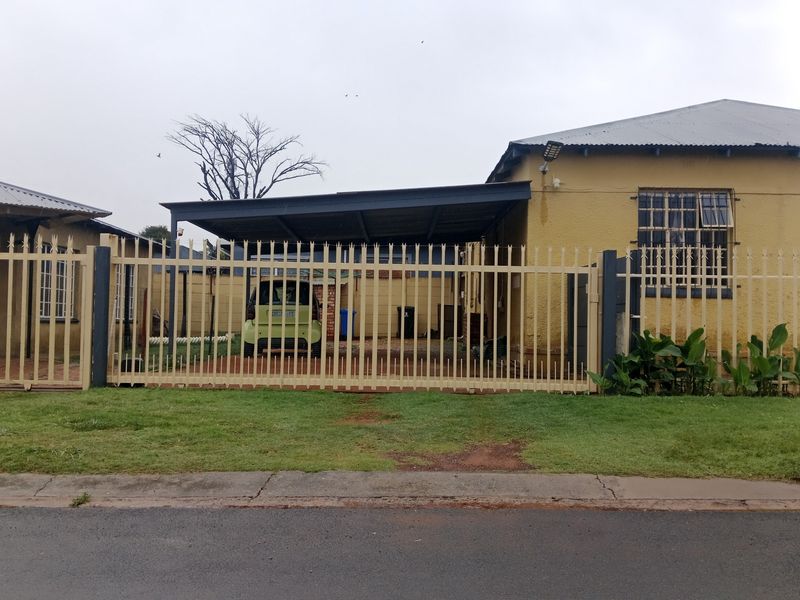Front view of a house featuring a metal security fence, a carport, and security bars on the windows.