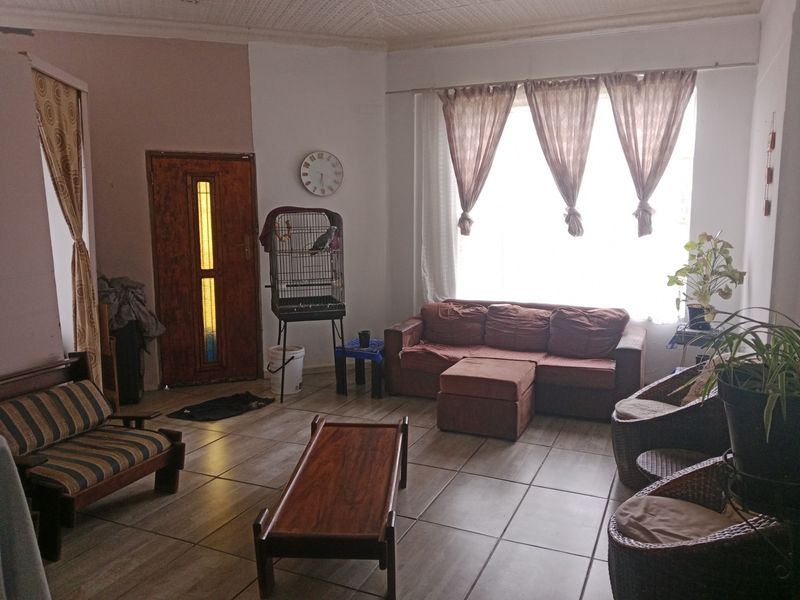 A living room featuring tiled flooring, a timber entrance door, and a large window providing natural light.