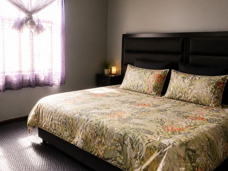 A well-lit bedroom featuring patterned carpet flooring, neutral grey walls, and a window with natural light.