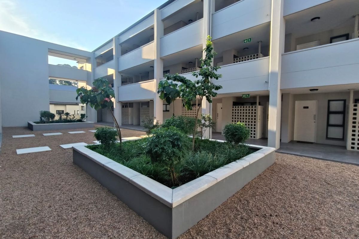 A well-maintained apartment complex courtyard featuring modern concrete planter boxes, gravel landscaping, and multi-story building facades with external access walkways.