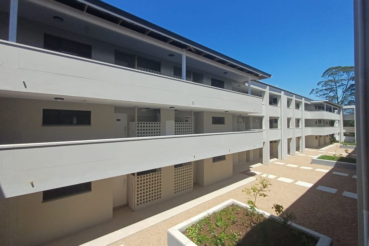 A modern multi-story apartment complex featuring clean architectural lines, concrete walkways, and well-maintained landscaped garden beds in the central courtyard area.