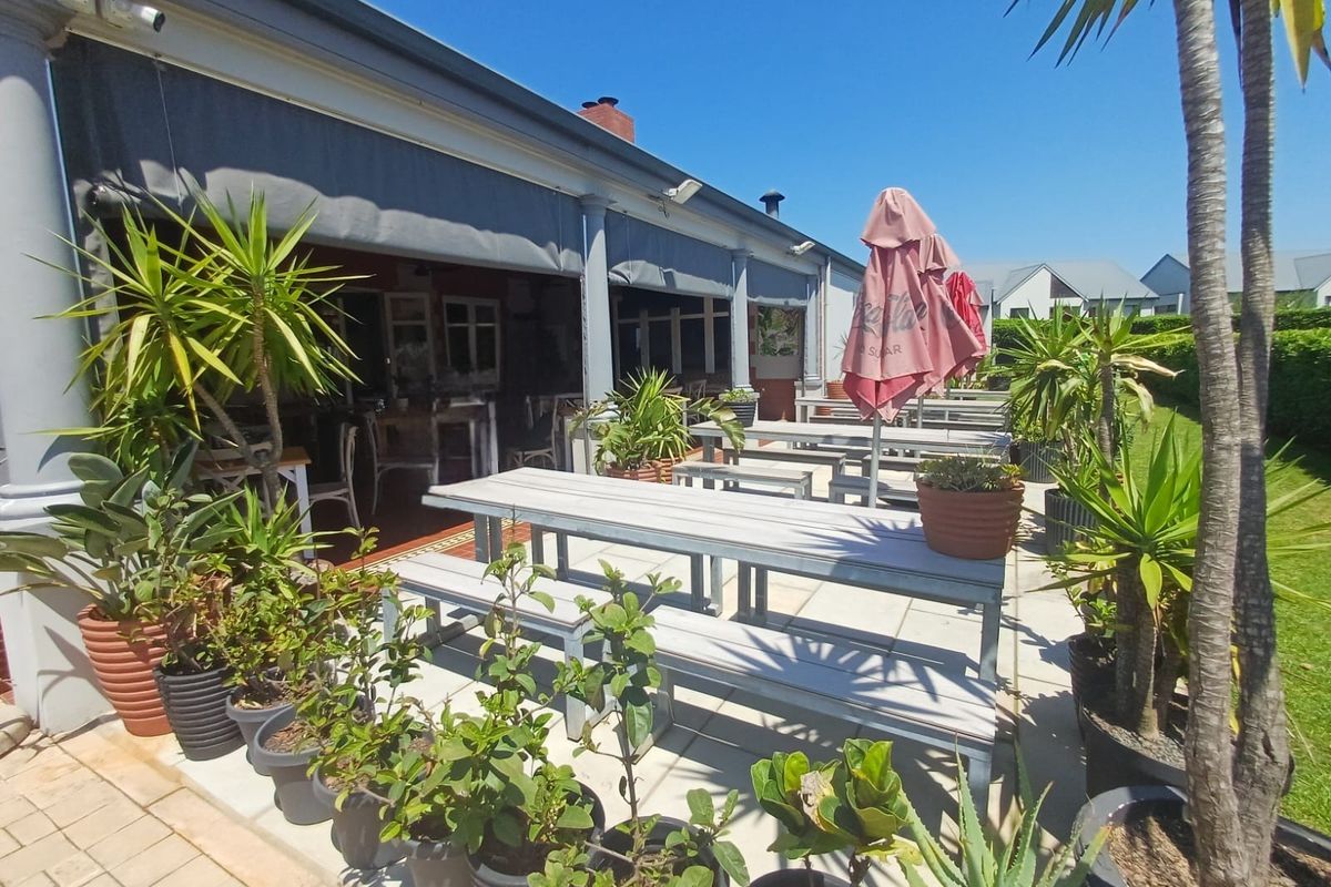 A spacious paved outdoor patio area featuring a retractable awning and structural columns, providing a comfortable space for outdoor dining and relaxation.