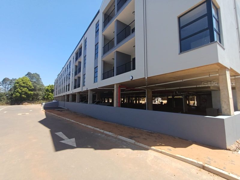 Modern apartment building exterior featuring multi-level balconies and an open-plan undercover parking area at ground level.