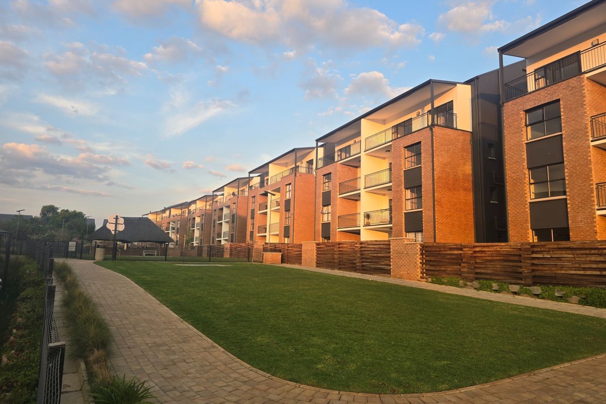 Exterior view of a modern multi-story apartment complex featuring brick facades, private balconies, and a well-maintained communal garden with paved walkways.