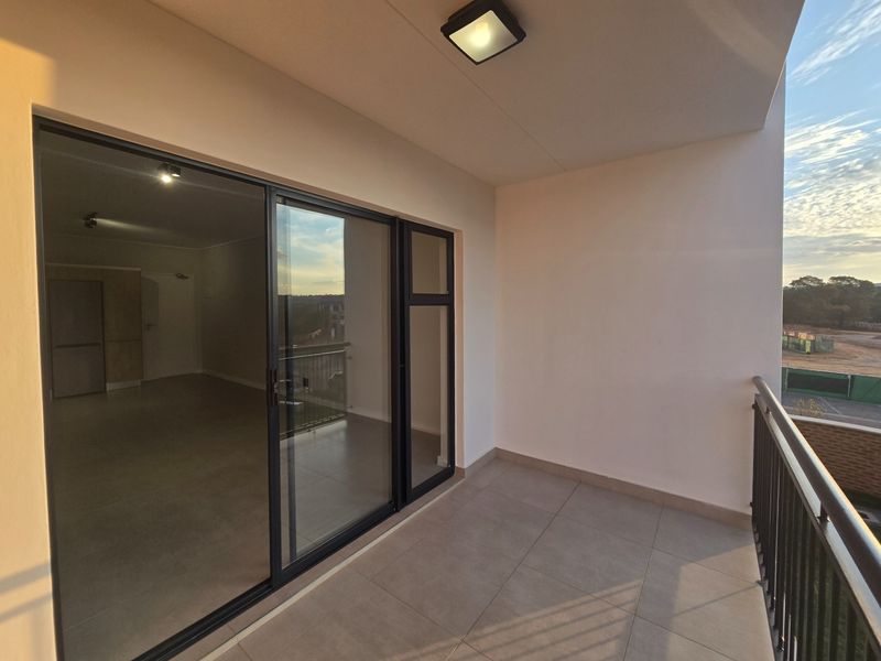 A clean, modern balcony featuring tiled flooring, a metal balustrade, and large sliding glass doors providing access to the interior living space.