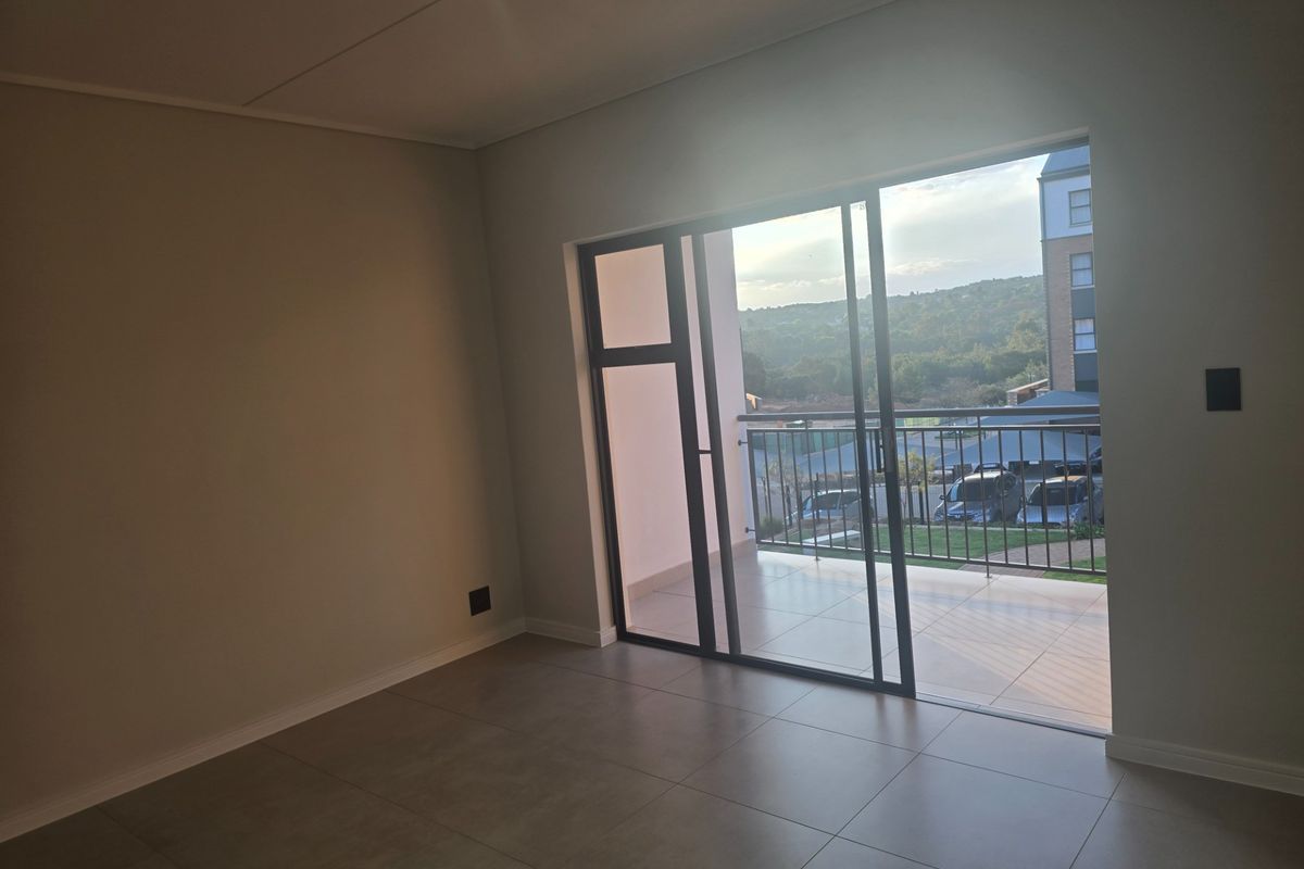 An empty, modern living area featuring large sliding glass doors that open onto a private balcony with scenic views.