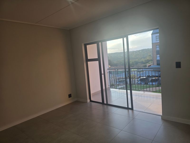 An empty, modern living area featuring large sliding glass doors that open onto a private balcony with scenic views.