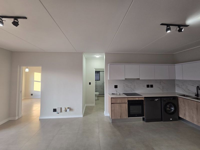 Modern open-plan kitchen featuring sleek cabinetry, integrated appliances, and marble-look splashbacks, seamlessly flowing into the living area with contemporary track lighting.