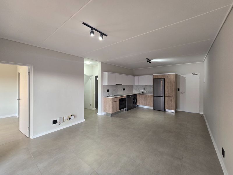 Modern open-plan kitchen featuring contemporary two-tone cabinetry, integrated appliances, and sleek tiled flooring in a spacious, well-lit living area.