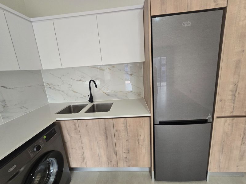 Modern kitchen featuring wood-grain and white cabinetry, stone countertops, marble-look splashback, and a sleek black mixer tap with integrated laundry facilities.