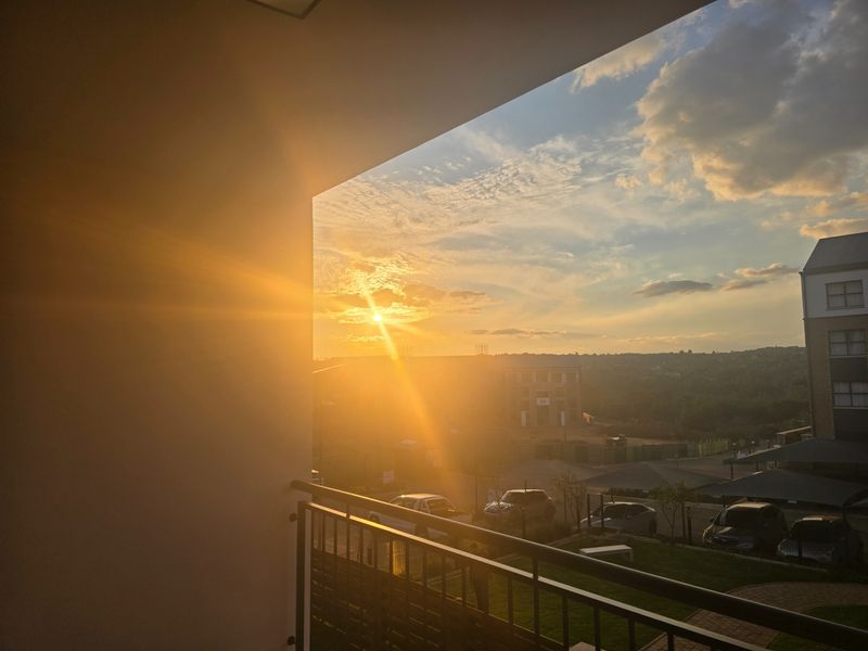 A scenic sunset view from an apartment balcony overlooking the surrounding neighborhood and parking area.