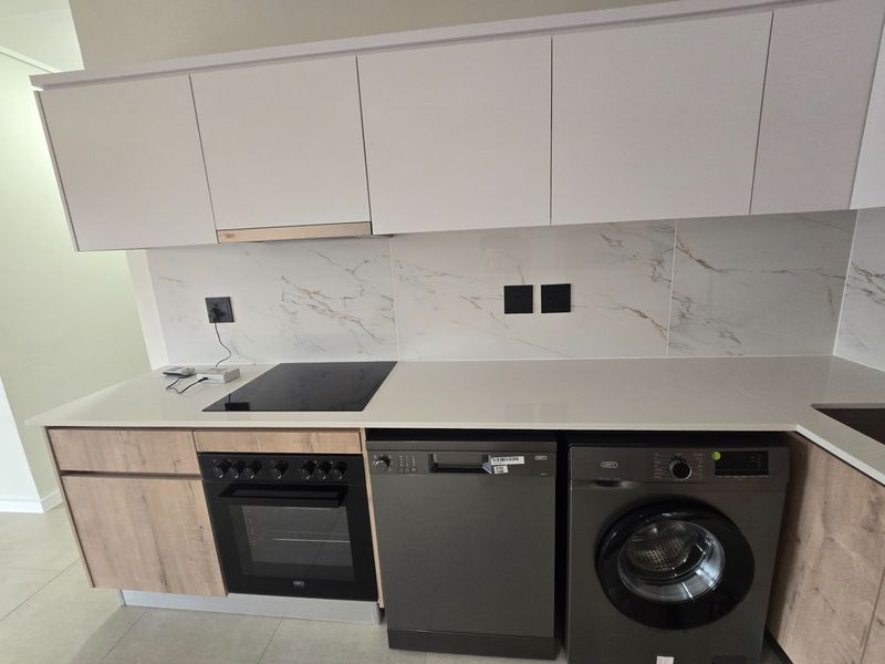 Modern kitchen featuring white cabinetry, marble-look splashback, quartz countertops, and integrated appliances including an oven, hob, dishwasher, and washing machine.