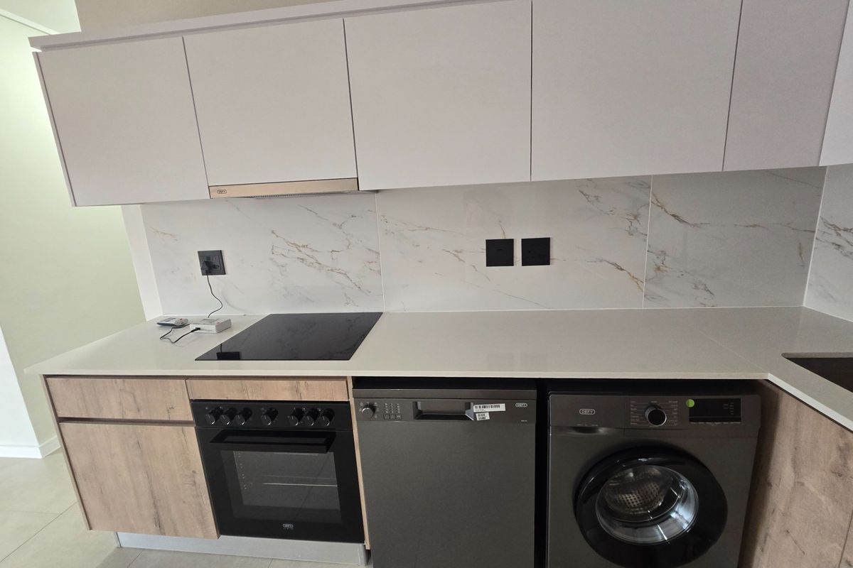 Modern kitchen featuring white cabinetry, marble-look splashback, quartz countertops, and integrated appliances including an oven, hob, dishwasher, and washing machine.