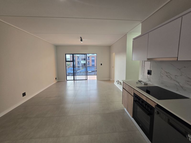 Modern open-plan living area featuring tiled floors, a sleek kitchen with built-in appliances, and a sliding door leading to a balcony.