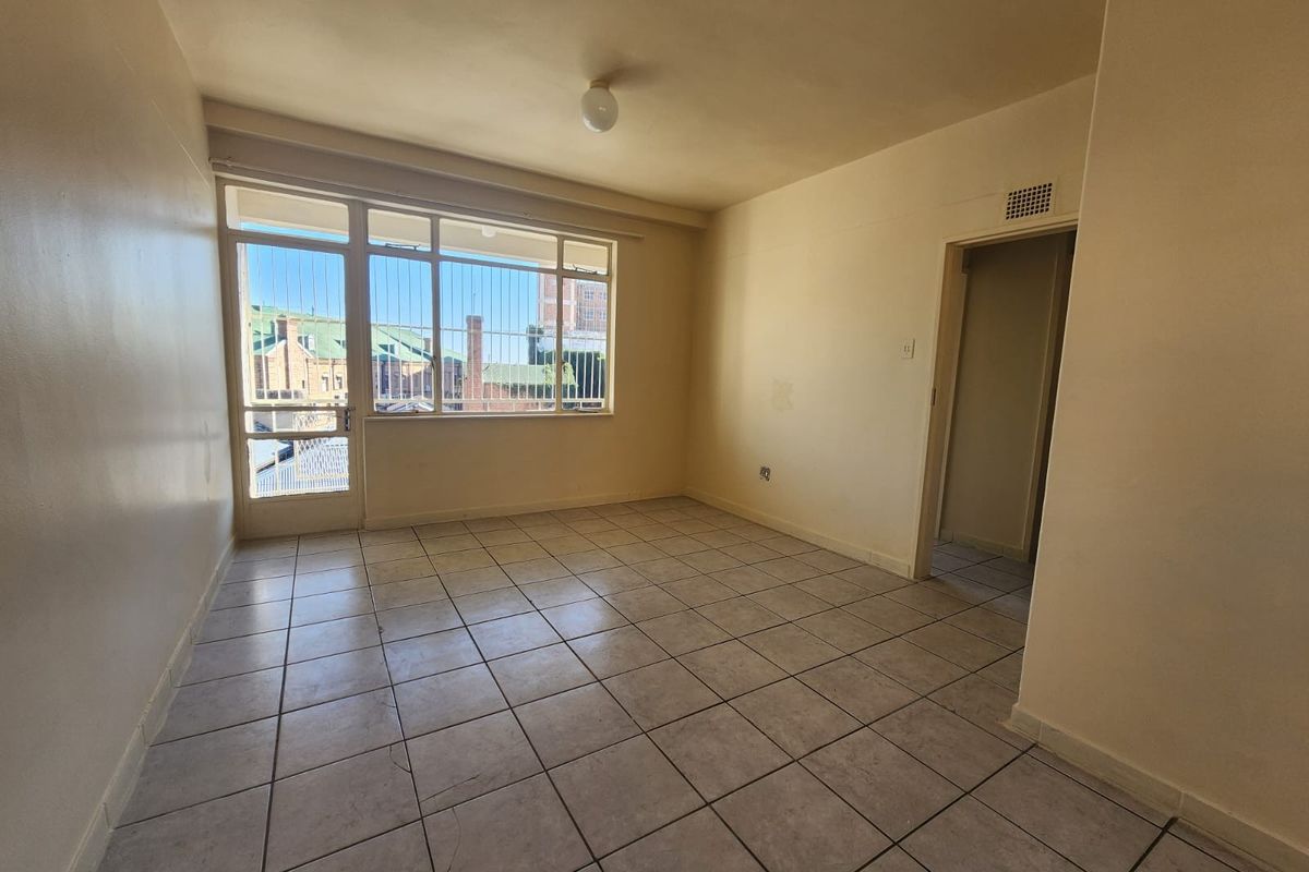 An empty living room featuring tiled flooring, large windows with security bars, and access to an outdoor area.