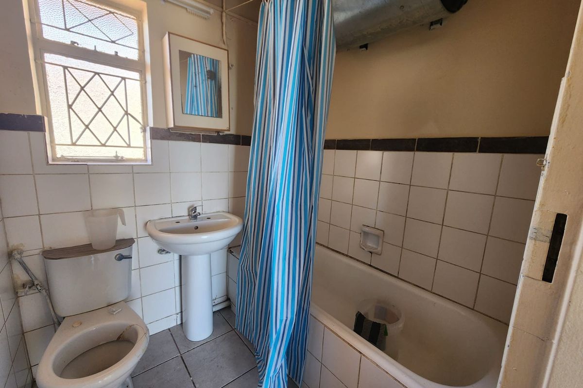A dated bathroom featuring a pedestal basin, toilet, and bathtub with tiled finishes. The space requires modernization and cosmetic updates.