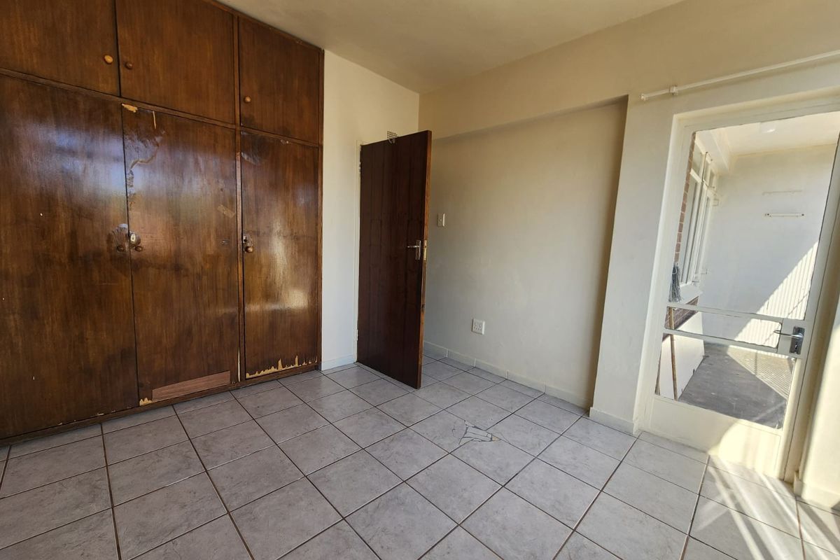 An empty bedroom featuring tiled flooring, built-in wooden cupboards, and direct access to an adjacent balcony area.