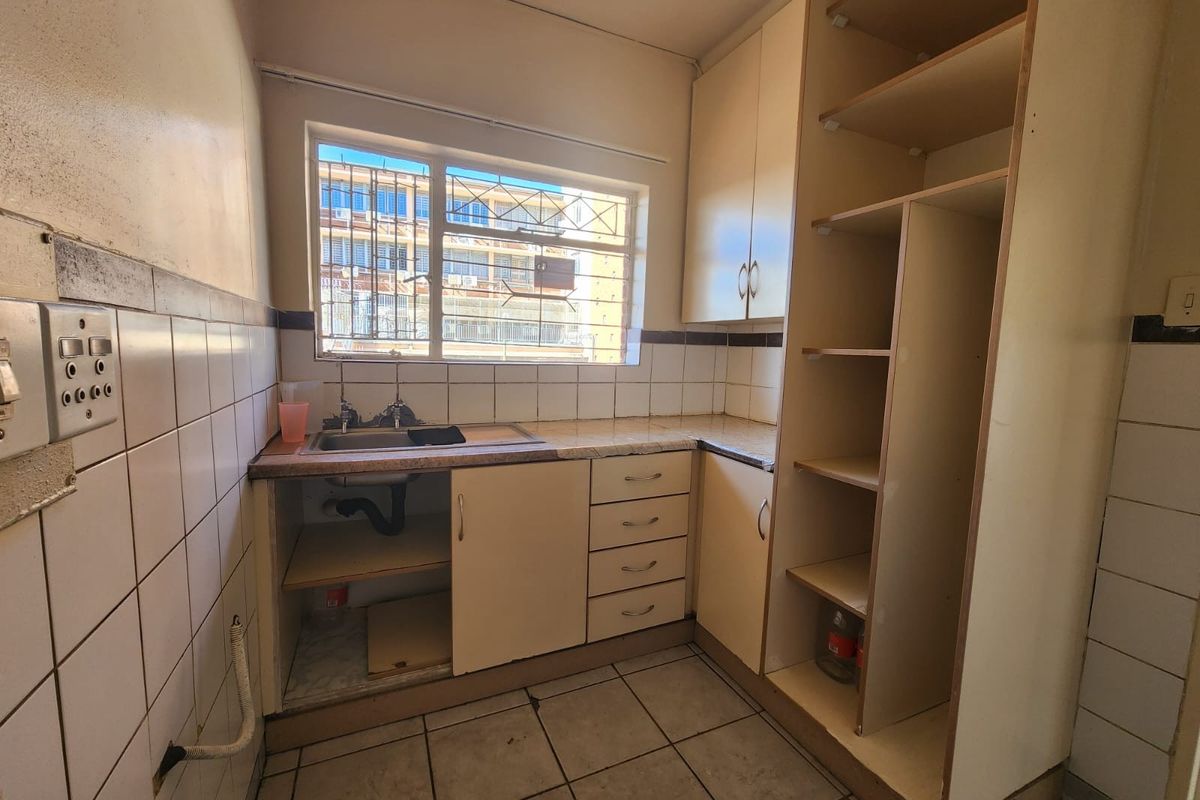 A dated kitchen featuring built-in cabinetry, a stainless steel sink, and tiled finishes, currently vacant and in need of cosmetic updates.