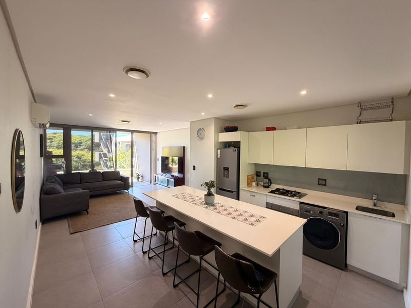 Modern open-plan living area featuring a sleek kitchen with a central island, gas hob, and seamless flow to the outdoor patio through sliding doors.