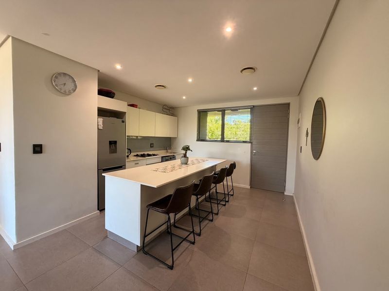 Modern kitchen featuring a central island with breakfast bar seating, sleek cabinetry, stone countertops, and recessed lighting, finished with neutral floor tiles.