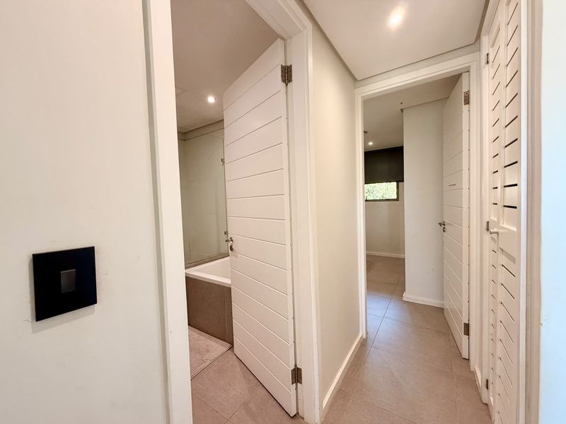 A bright, modern hallway featuring tiled flooring, recessed lighting, and access to adjacent rooms through clean, horizontal panel doors.
