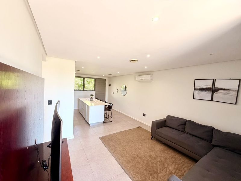 Spacious open-plan living and kitchen area featuring tiled floors, recessed lighting, and a central kitchen island, creating a bright and functional living space.
