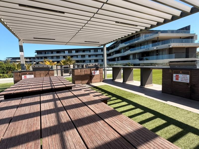 A modern outdoor entertainment area featuring a large pergola, built-in braai stations, and a spacious dining area with artificial turf.