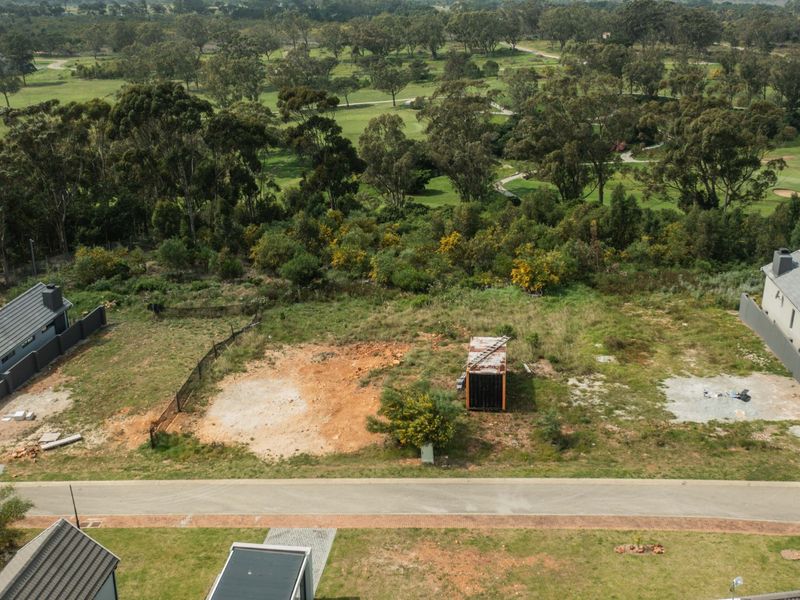 Aerial view of a vacant residential plot situated in a developed estate, featuring road access and surrounding natural landscape.