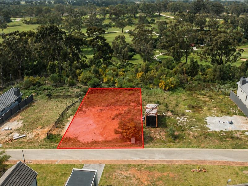 Aerial view of a vacant residential plot situated in a developed estate, bordering a golf course and adjacent to existing modern homes.