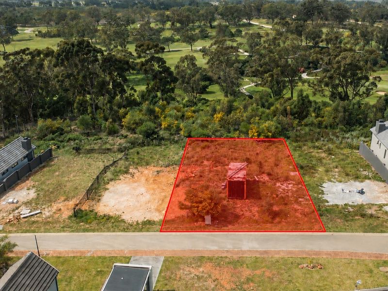 Aerial view of a vacant residential plot highlighted in red, situated in a developed estate with surrounding greenery.