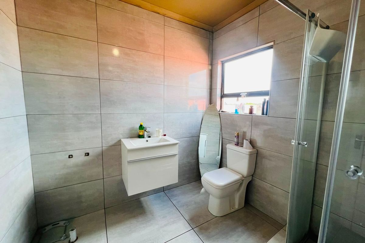 A modern bathroom featuring large-format grey wall tiles, a wall-mounted vanity, a toilet, and a glass-enclosed shower.