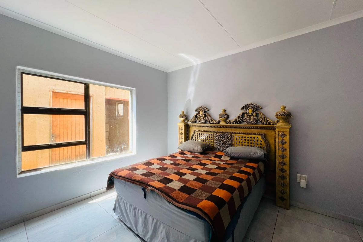 A bedroom featuring neutral wall paint, tiled flooring, and an aluminium-framed window providing natural light.