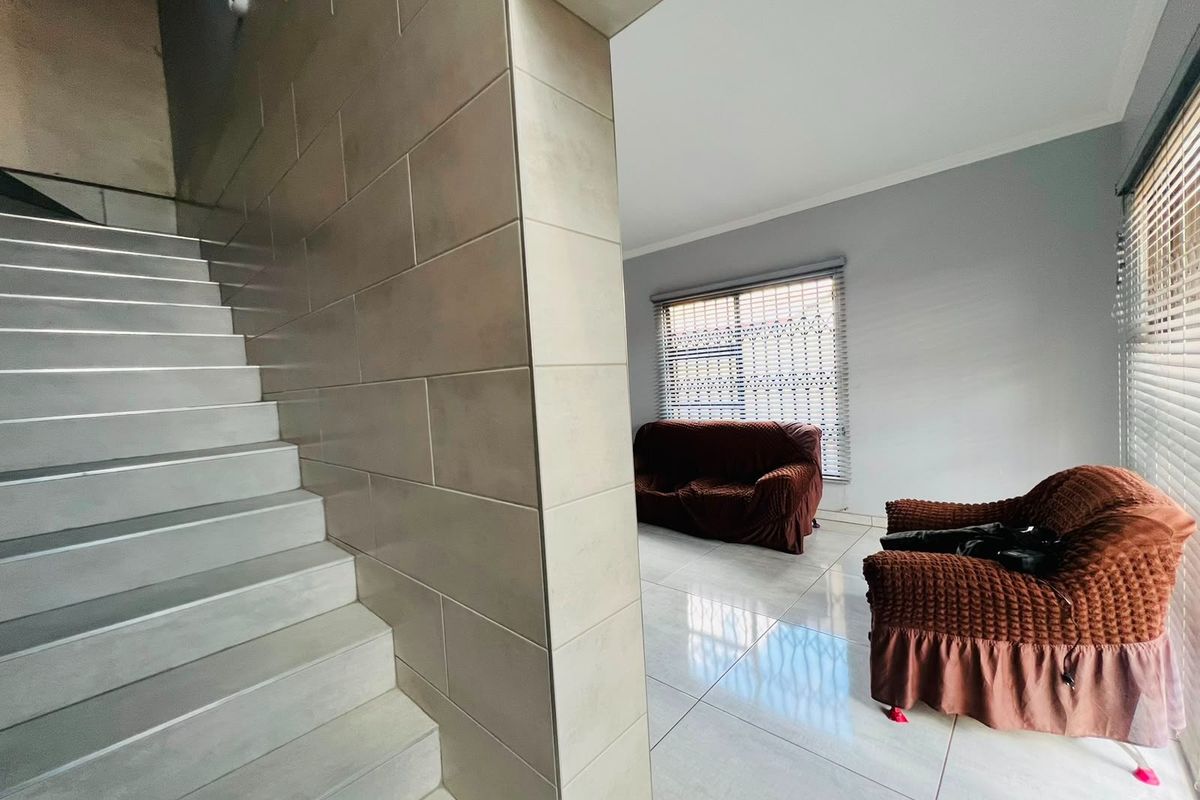 A bright living area featuring modern tiled flooring, a tiled staircase, and large windows with venetian blinds.