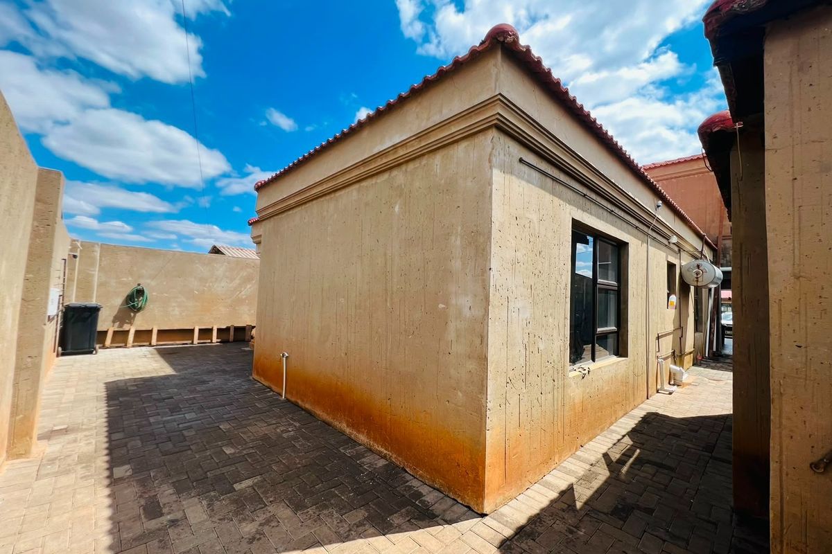 Rear exterior view of the property featuring a paved courtyard and showing significant signs of rising damp and weathering on the exterior walls.