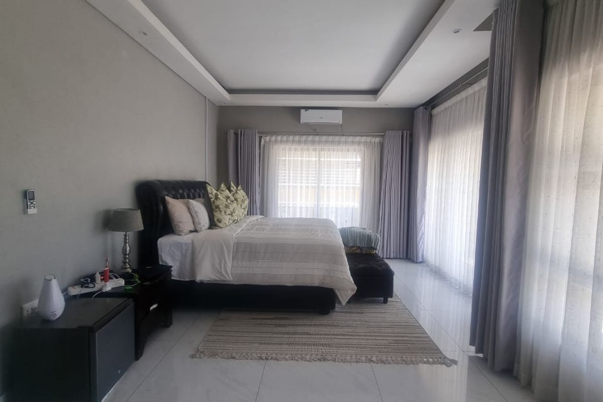 Spacious bedroom featuring tiled flooring, recessed ceiling detail, split-system air conditioning, and large sliding glass doors with floor-to-ceiling curtains.