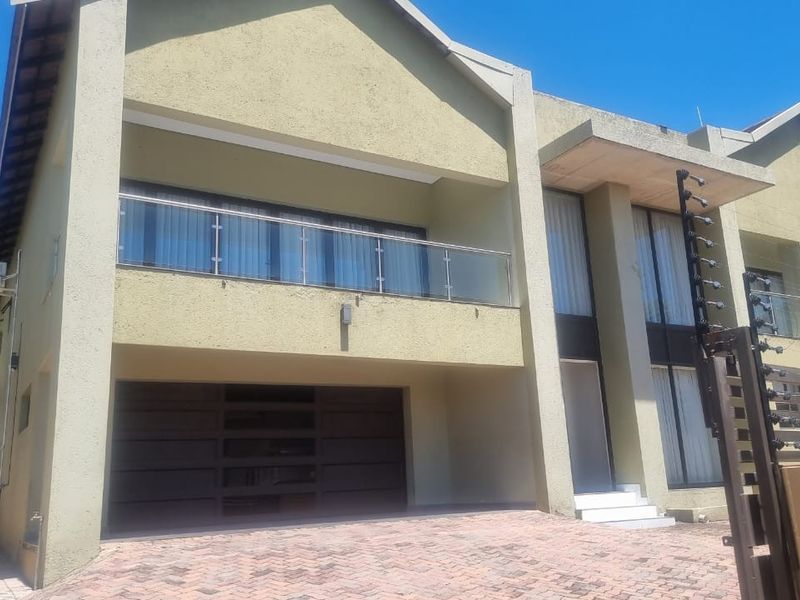 Modern double-story residential facade featuring a double garage, upper-level balcony with glass balustrade, and paved driveway access.