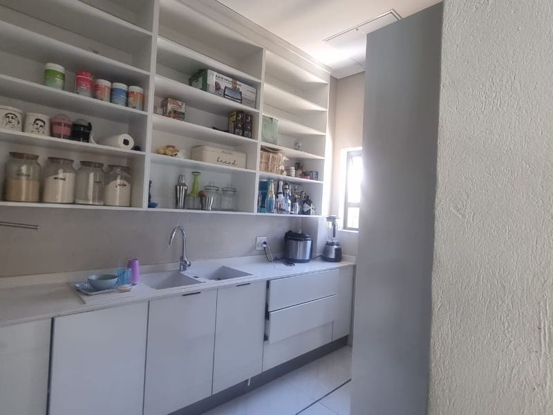 A functional scullery featuring extensive open shelving, modern white cabinetry, stone countertops, and a double sink with a mixer tap.