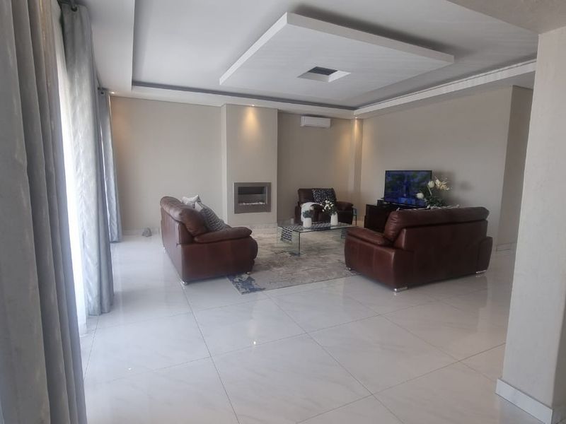 Spacious living room featuring a modern recessed ceiling, built-in fireplace, wall-mounted air conditioning unit, and polished tiled flooring.