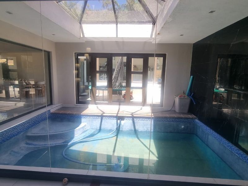 An indoor swimming pool area featuring a large skylight, glass wall enclosures, and tiled finishes, providing a bright and enclosed aquatic space.