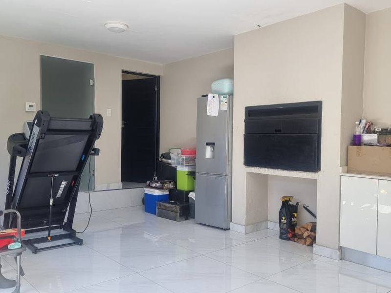 Covered patio area featuring a built-in braai, kitchenette cabinetry with a sink, and modern tiled flooring.