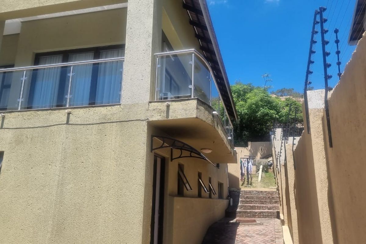 Rear exterior view of the property featuring a glass balustrade balcony, paved walkway, brick stairs, and perimeter electric fencing.