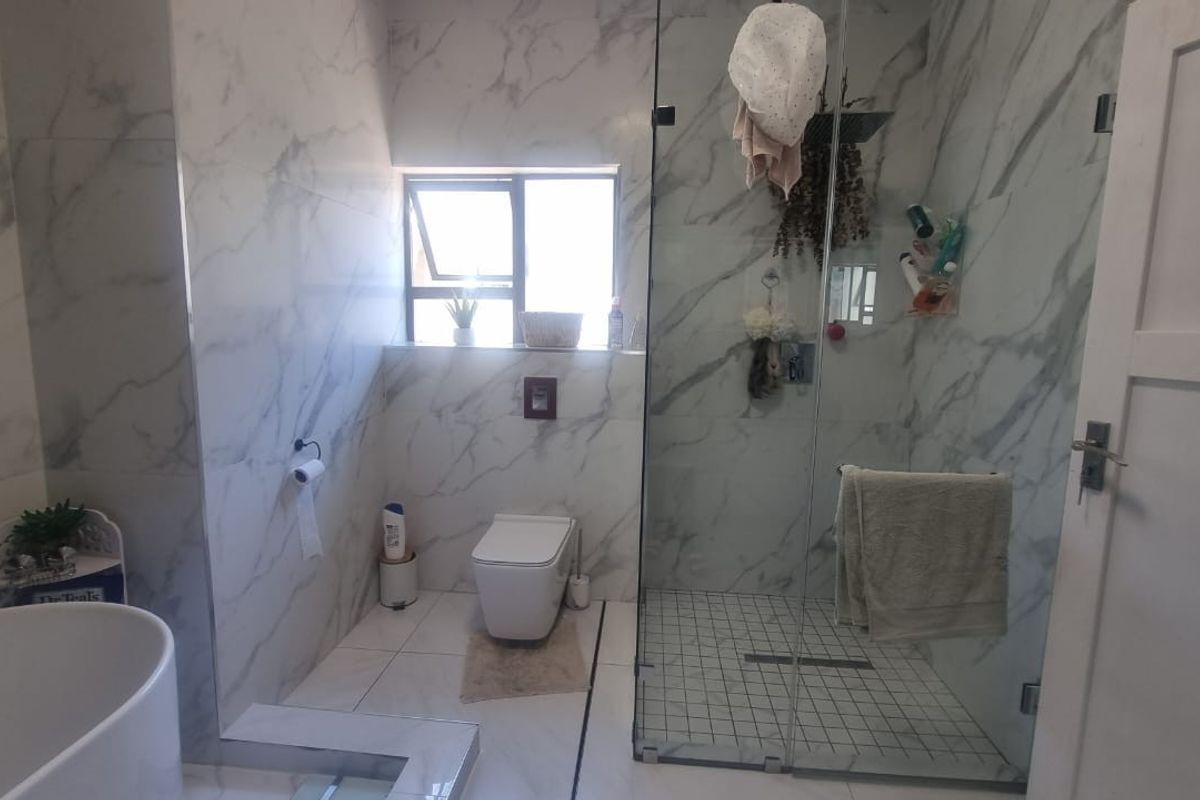 Modern bathroom featuring marble-look wall tiles, a freestanding bathtub, a wall-hung toilet, and a spacious glass-enclosed shower with a rain shower head.