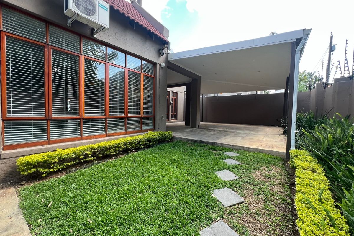 A well-maintained rear exterior featuring a covered patio, paved flooring, a small lawn, and secure boundary walls with electric fencing.