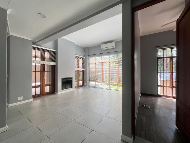 Spacious open-plan living area featuring large windows, tiled flooring, a built-in fireplace, and a wall-mounted air conditioning unit.