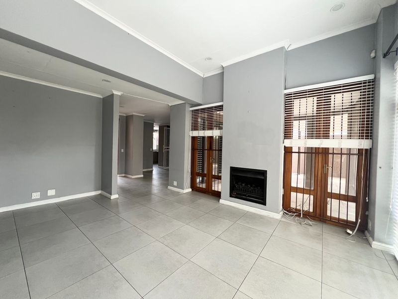 Spacious living area featuring large format floor tiles, a built-in fireplace, and wooden framed glass doors leading to the exterior.