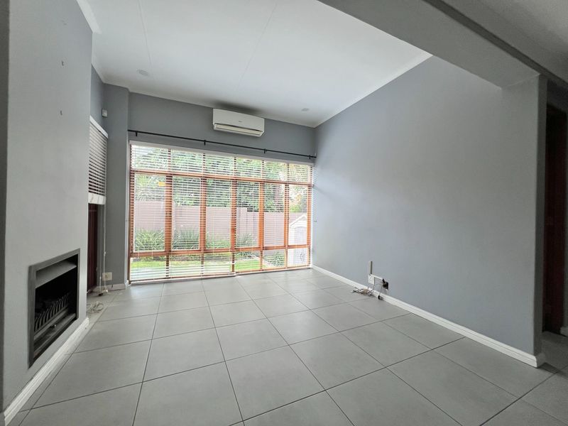 A bright, empty living room featuring large windows, tiled flooring, a built-in fireplace, and a wall-mounted air conditioning unit.