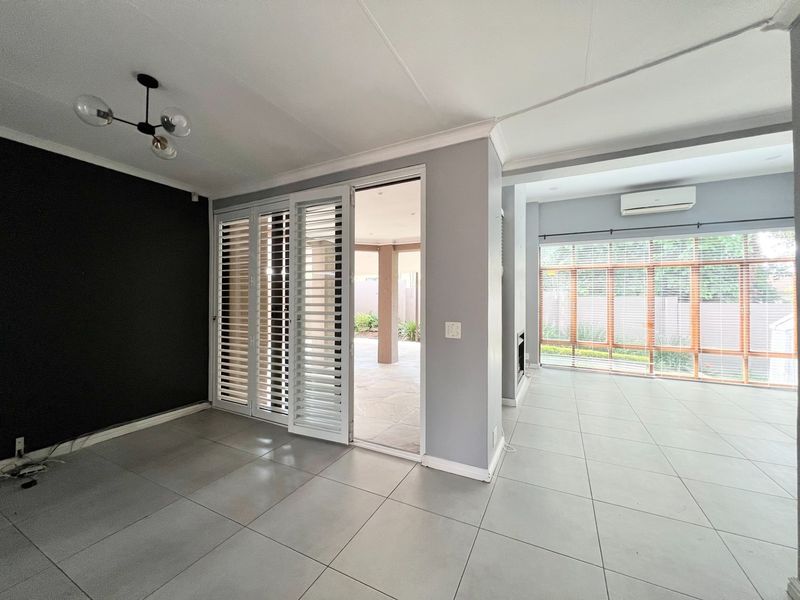 Spacious open-plan living area featuring large windows, tiled flooring, a built-in fireplace, and direct access to an outdoor patio through sliding shutters.
